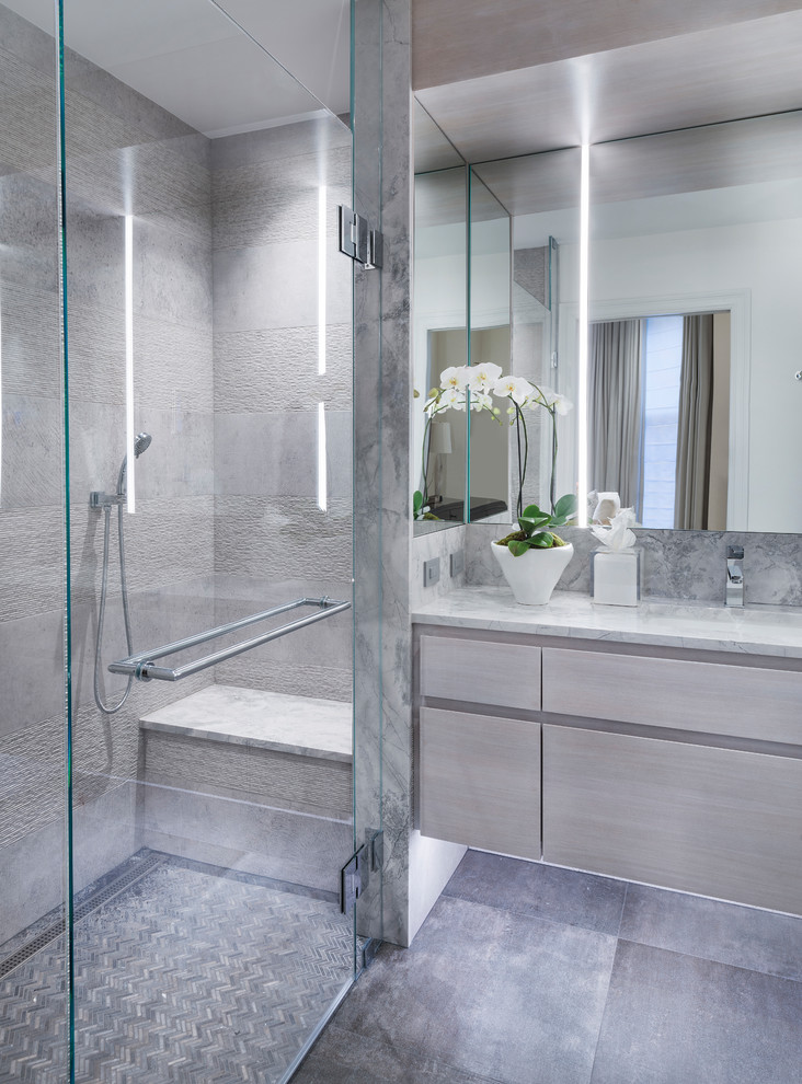 Inredning av ett modernt grå grått badrum, med släta luckor, skåp i ljust trä, en kantlös dusch, grå kakel, grå väggar, klinkergolv i porslin, ett integrerad handfat, grått golv och dusch med gångjärnsdörr