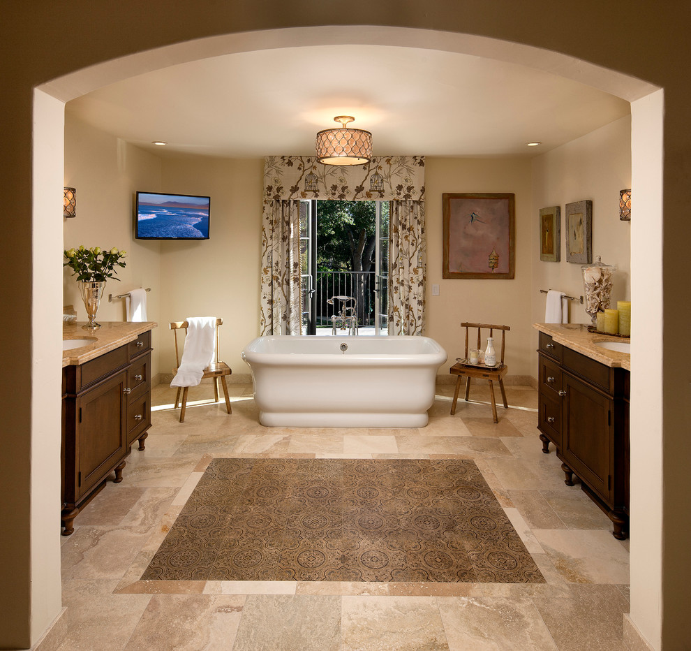 This is an example of a mediterranean bathroom in Santa Barbara with a submerged sink, dark wood cabinets, a freestanding bath, beige tiles and recessed-panel cabinets.