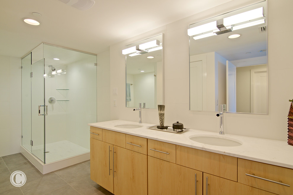 Пример оригинального дизайна: ванная комната среднего размера в современном стиле с плоскими фасадами, светлыми деревянными фасадами, ванной в нише, угловым душем, унитазом-моноблоком, белой плиткой, керамогранитной плиткой, белыми стенами, полом из керамогранита, врезной раковиной и мраморной столешницей