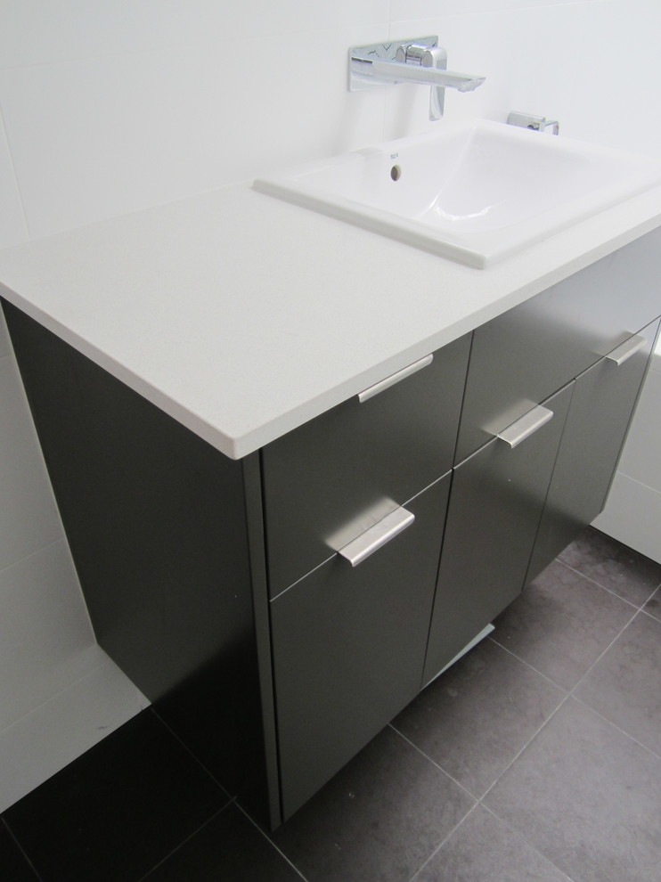 This is an example of a small modern bathroom in Sydney with a built-in sink, flat-panel cabinets, black cabinets, engineered stone worktops, an alcove bath, a shower/bath combination, white tiles, ceramic tiles, white walls and ceramic flooring.