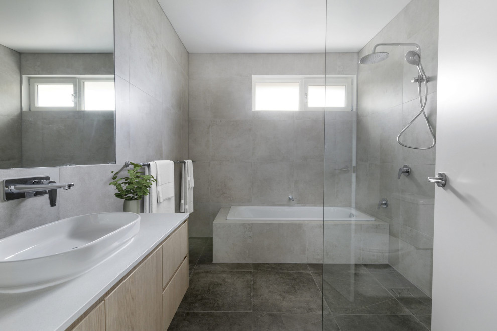 Exempel på ett modernt vit vitt badrum, med släta luckor, skåp i ljust trä, ett platsbyggt badkar, våtrum, grå kakel, ett fristående handfat och grått golv