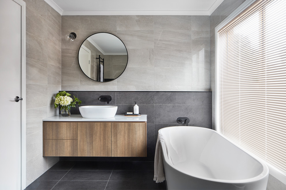 Inspiration for a contemporary master gray tile gray floor freestanding bathtub remodel in Melbourne with flat-panel cabinets, medium tone wood cabinets, gray walls, a vessel sink and white countertops