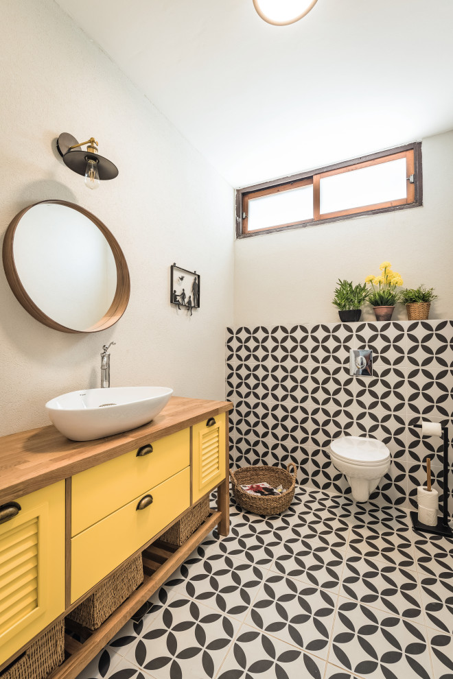 Inspiration för ett nordiskt brun brunt badrum med dusch, med luckor med lamellpanel, gula skåp, svart och vit kakel, vita väggar, ett fristående handfat, träbänkskiva och flerfärgat golv