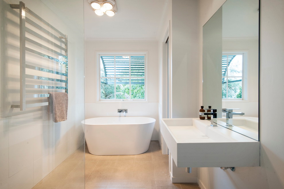 Ejemplo de cuarto de baño actual de tamaño medio con lavabo suspendido, encimera de acrílico, bañera exenta, baldosas y/o azulejos blancos, paredes blancas y aseo y ducha