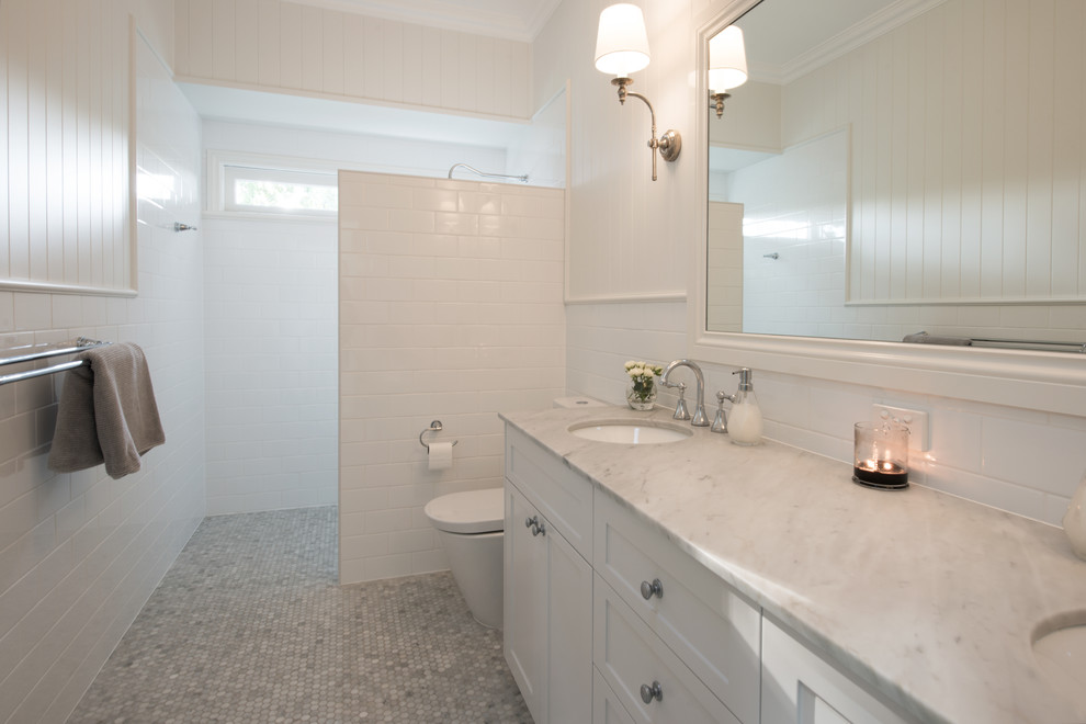 Exemple d'une salle de bain principale chic avec un placard à porte shaker, des portes de placard blanches, un carrelage blanc, un carrelage métro et un plan de toilette en marbre.