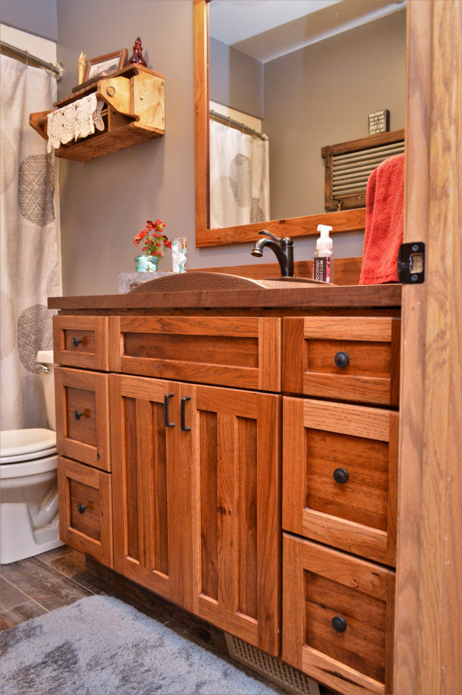 Inspiration for a medium sized rustic family bathroom in Chicago with shaker cabinets, medium wood cabinets, a shower/bath combination, blue walls, laminate floors, a built-in sink, wooden worktops, brown floors, a shower curtain, brown worktops and a two-piece toilet.