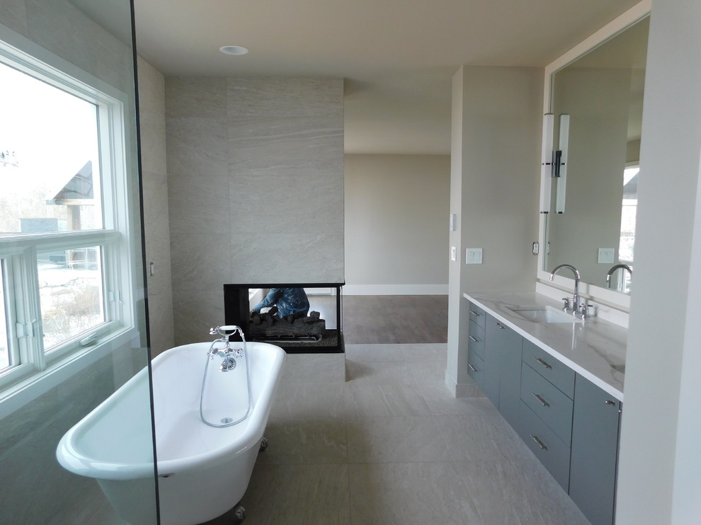 Cette image montre une salle de bain minimaliste avec un placard à porte plane, des portes de placard grises, une baignoire indépendante, une douche d'angle, WC à poser, un carrelage blanc, des carreaux de miroir, un mur gris, un sol en marbre, un lavabo encastré, un plan de toilette en granite, un sol gris et une cabine de douche à porte battante.