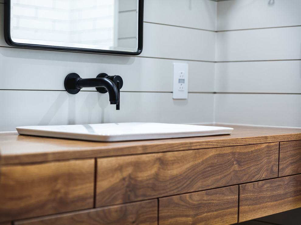 Bild på ett mellanstort lantligt badrum, med möbel-liknande, skåp i mellenmörkt trä, ett badkar i en alkov, en dusch/badkar-kombination, en toalettstol med separat cisternkåpa, vit kakel, keramikplattor, grå väggar, klinkergolv i porslin, träbänkskiva, grått golv, dusch med duschdraperi och ett fristående handfat