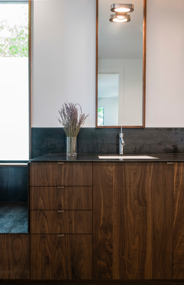 Diseño de cuarto de baño principal actual de tamaño medio con puertas de armario de madera en tonos medios, lavabo bajoencimera, encimeras grises, armarios con paneles lisos, baldosas y/o azulejos grises y paredes blancas