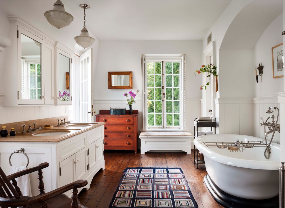 Foto de cuarto de baño clásico con armarios con paneles empotrados, puertas de armario blancas, bañera exenta, paredes blancas y suelo de madera oscura