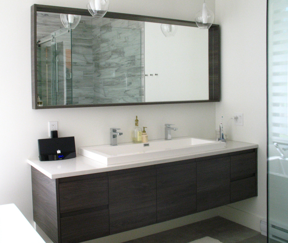 This is an example of a medium sized contemporary ensuite bathroom in Montreal with flat-panel cabinets, dark wood cabinets, a freestanding bath, a double shower, a one-piece toilet, white tiles, stone slabs, white walls, dark hardwood flooring, engineered stone worktops and an integrated sink.