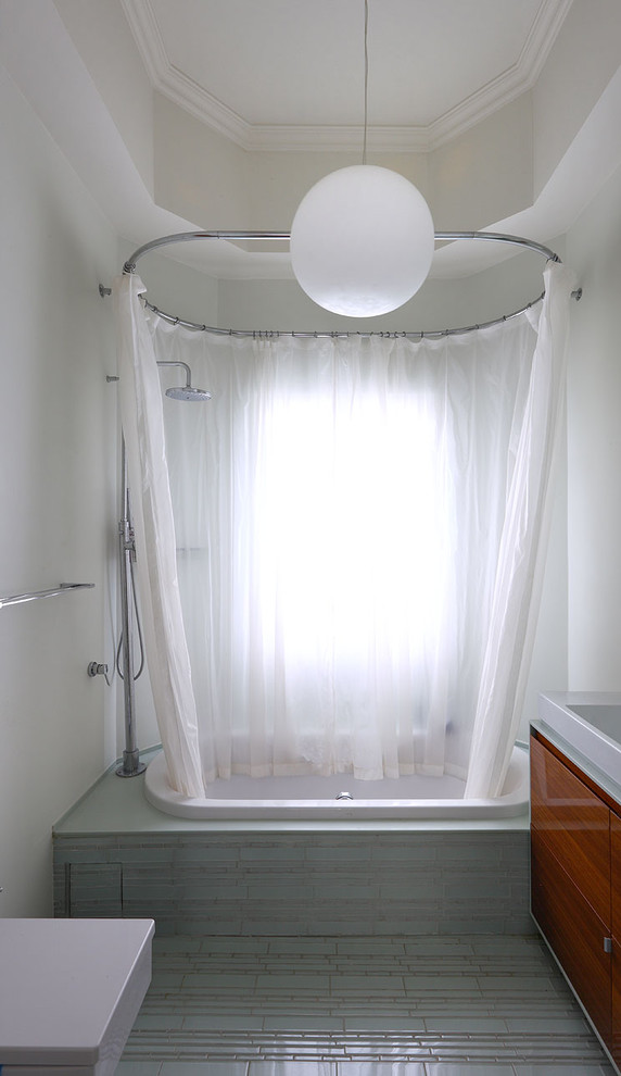 Cette image montre une salle de bain minimaliste en bois foncé de taille moyenne avec un placard à porte plane, une baignoire en alcôve, un combiné douche/baignoire, WC suspendus, un carrelage gris, un carrelage en pâte de verre, un mur blanc, un sol en carrelage de terre cuite, une vasque et un plan de toilette en surface solide.