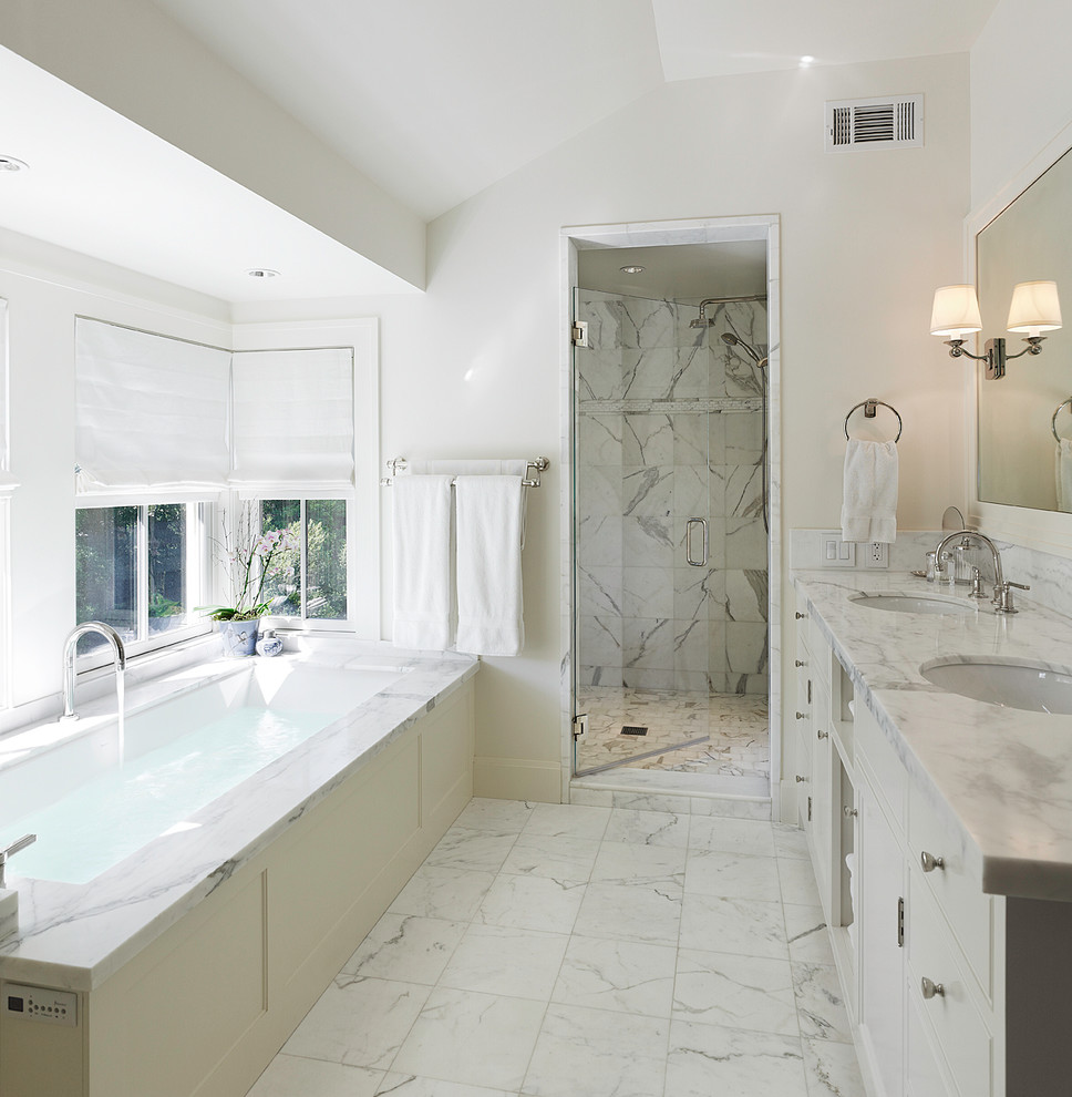 Foto på ett vintage badrum, med ett undermonterad handfat, vita skåp, ett undermonterat badkar, en dusch i en alkov, vit kakel, stenkakel, vita väggar och bänkskiva i kalksten