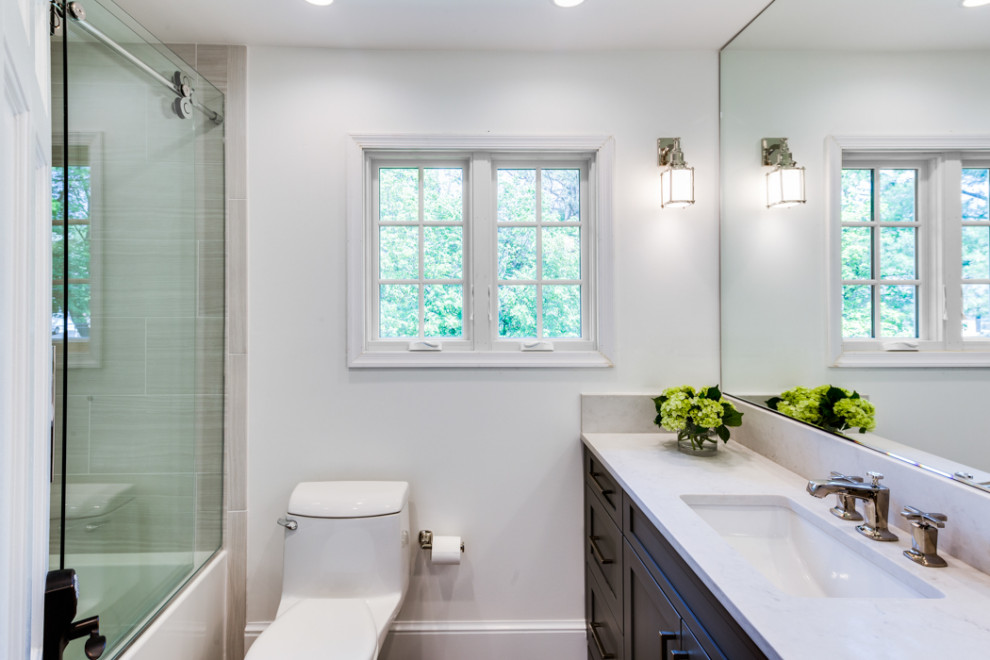 Стильный дизайн: ванная комната среднего размера в стиле неоклассика (современная классика) с плоскими фасадами, серыми фасадами, накладной ванной, душем в нише, унитазом-моноблоком, белой плиткой, керамической плиткой, белыми стенами, полом из ламината, накладной раковиной, мраморной столешницей, коричневым полом, душем с раздвижными дверями, белой столешницей, тумбой под одну раковину и напольной тумбой - последний тренд