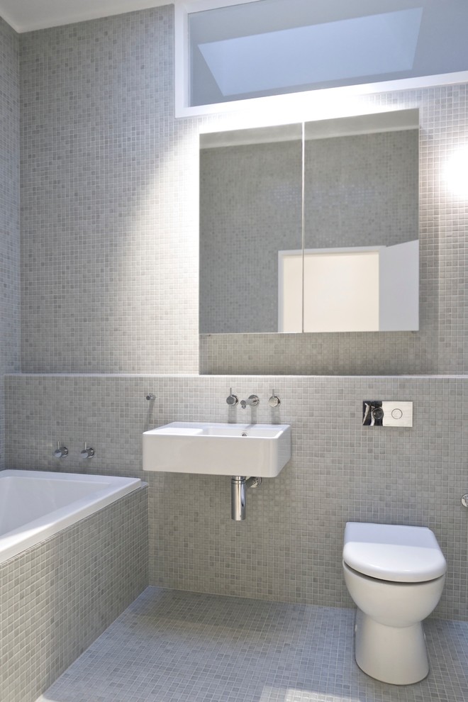 Imagen de cuarto de baño moderno con lavabo suspendido, bañera empotrada, baldosas y/o azulejos grises, baldosas y/o azulejos en mosaico, suelo con mosaicos de baldosas, sanitario de pared y paredes grises