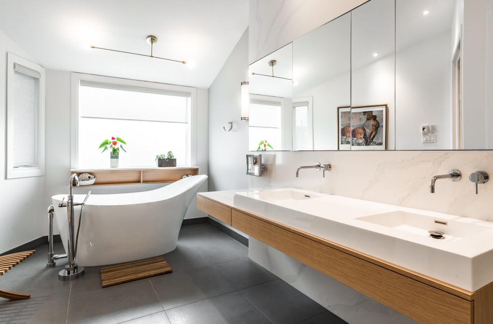 Idéer för ett stort minimalistiskt vit en-suite badrum, med släta luckor, skåp i ljust trä, ett fristående badkar, en dusch i en alkov, en vägghängd toalettstol, vit kakel, stenhäll, grå väggar, klinkergolv i keramik, ett integrerad handfat, bänkskiva i akrylsten, brunt golv och dusch med skjutdörr