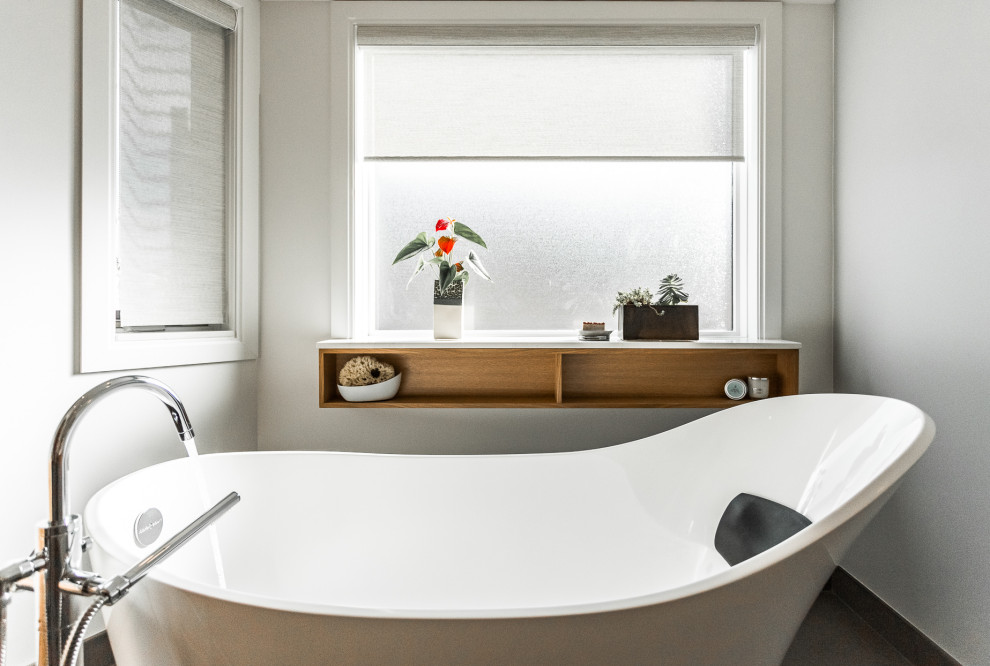 Bild på ett stort skandinaviskt vit vitt en-suite badrum, med släta luckor, skåp i ljust trä, ett fristående badkar, en dusch i en alkov, en vägghängd toalettstol, vit kakel, stenhäll, grå väggar, klinkergolv i keramik, ett integrerad handfat, bänkskiva i akrylsten, brunt golv och dusch med skjutdörr