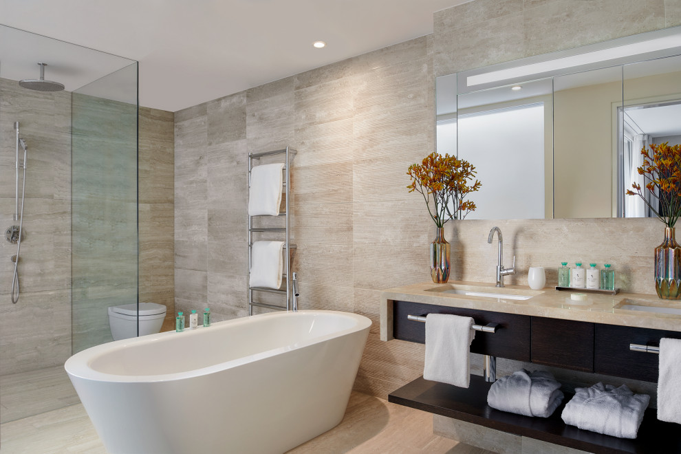 Contemporary ensuite bathroom in London with flat-panel cabinets, dark wood cabinets, a freestanding bath, a built-in shower, a wall mounted toilet, beige tiles, beige walls, a submerged sink, beige floors, beige worktops, double sinks and a floating vanity unit.