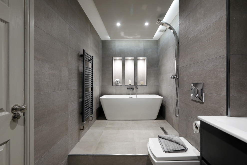 На фото: большая главная ванная комната в современном стиле с плоскими фасадами, черными фасадами, отдельно стоящей ванной, душевой комнатой, инсталляцией, серой плиткой, монолитной раковиной, серым полом, открытым душем, белой столешницей и нишей