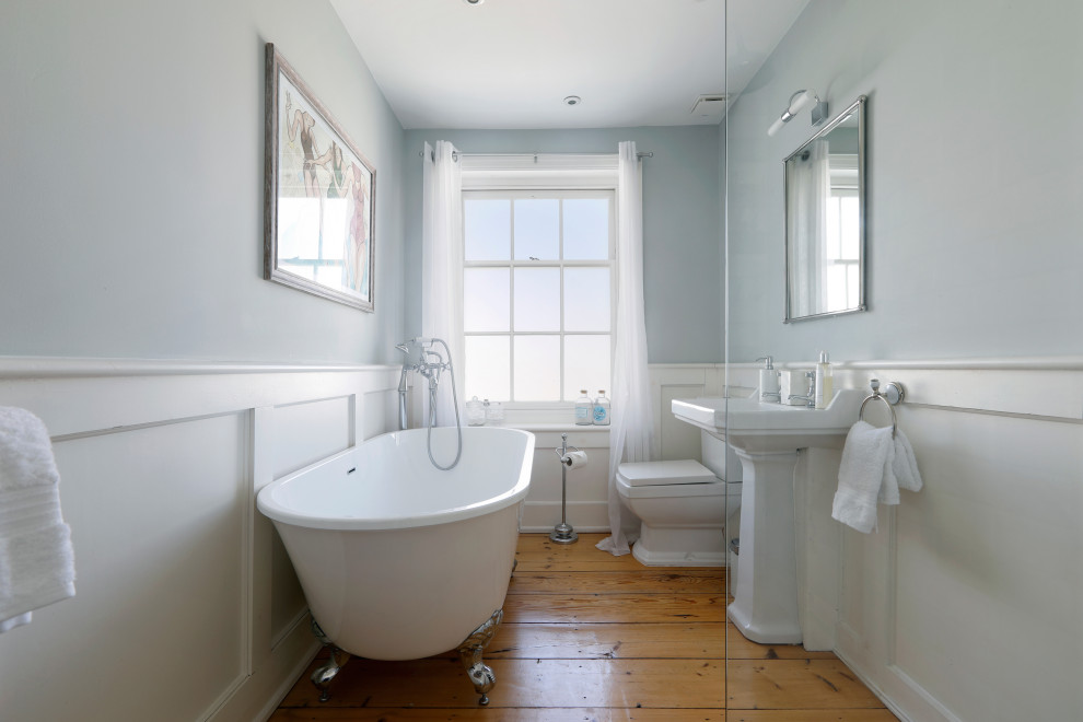 Klassisk inredning av ett mellanstort badrum för barn, med ett badkar med tassar, en öppen dusch, en toalettstol med separat cisternkåpa, mellanmörkt trägolv, ett konsol handfat, brunt golv, med dusch som är öppen och grå väggar