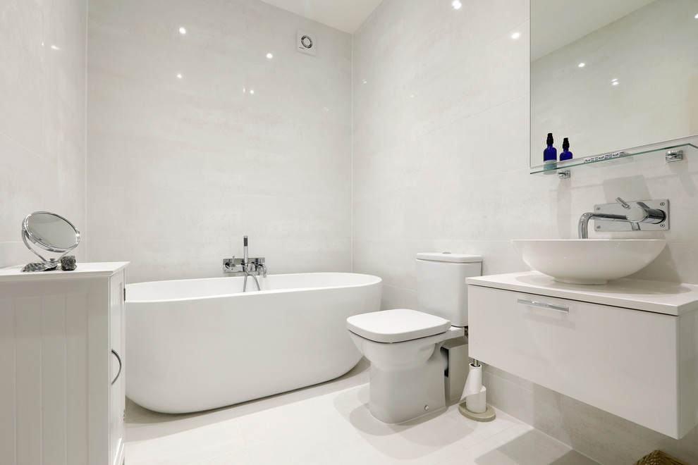 This is an example of a small contemporary family bathroom in Sussex with flat-panel cabinets, white cabinets, a freestanding bath, a shower/bath combination, a two-piece toilet, beige tiles, porcelain tiles, beige walls, porcelain flooring, a vessel sink, engineered stone worktops, beige floors and an open shower.