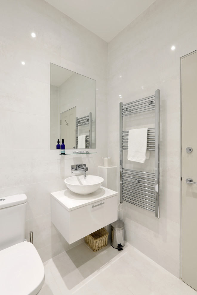 This is an example of a small contemporary family bathroom in Sussex with flat-panel cabinets, white cabinets, a freestanding bath, a shower/bath combination, a two-piece toilet, beige tiles, porcelain tiles, beige walls, porcelain flooring, a vessel sink, engineered stone worktops, beige floors and an open shower.