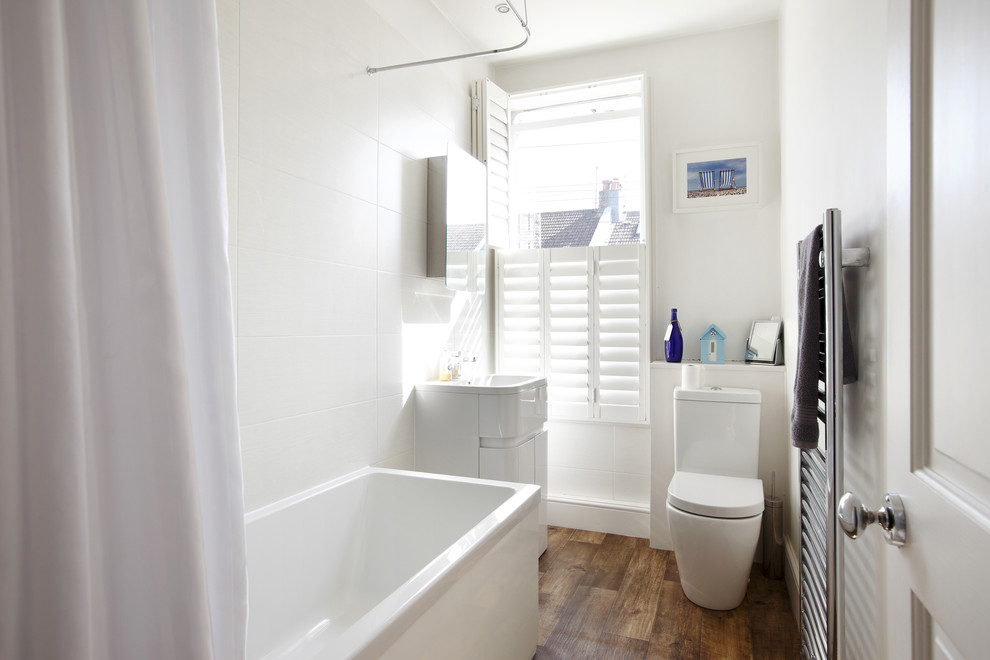 Design ideas for a small scandi family bathroom in Sussex with freestanding cabinets, white cabinets, a built-in bath, a shower/bath combination, a one-piece toilet, white tiles, ceramic tiles, white walls, laminate floors and a built-in sink.