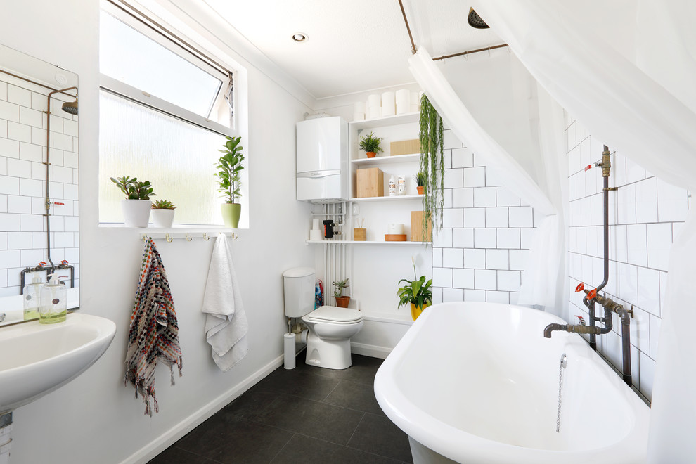 Photo of a medium sized urban family bathroom in Sussex with white cabinets, a claw-foot bath, a shower/bath combination, a two-piece toilet, white tiles, ceramic tiles, white walls, ceramic flooring, a wall-mounted sink, black floors and a shower curtain.