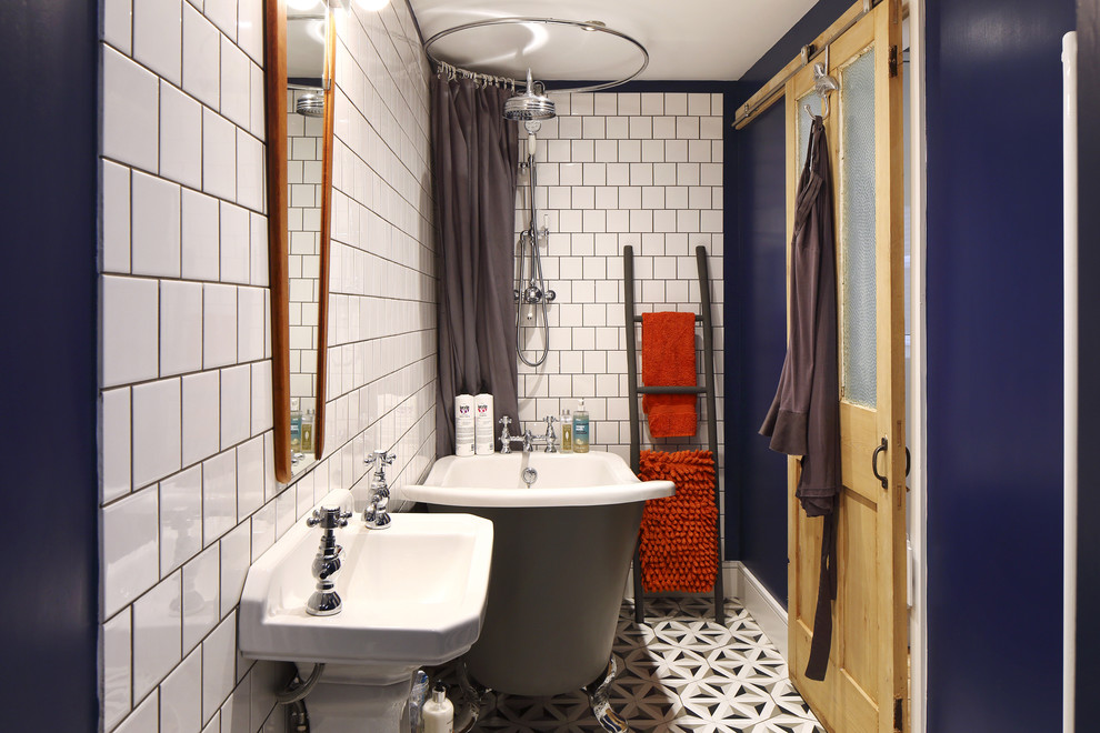 Inredning av ett nordiskt litet badrum för barn, med ett fristående badkar, en dusch/badkar-kombination, en toalettstol med hel cisternkåpa, vit kakel, tunnelbanekakel, blå väggar, klinkergolv i keramik och ett piedestal handfat