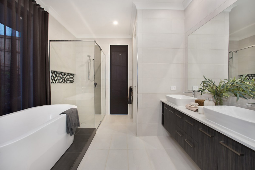 Стильный дизайн: большая главная ванная комната в современном стиле с плоскими фасадами, темными деревянными фасадами, отдельно стоящей ванной, угловым душем, белой плиткой, керамогранитной плиткой, белыми стенами, полом из керамогранита, настольной раковиной, белым полом и белой столешницей - последний тренд