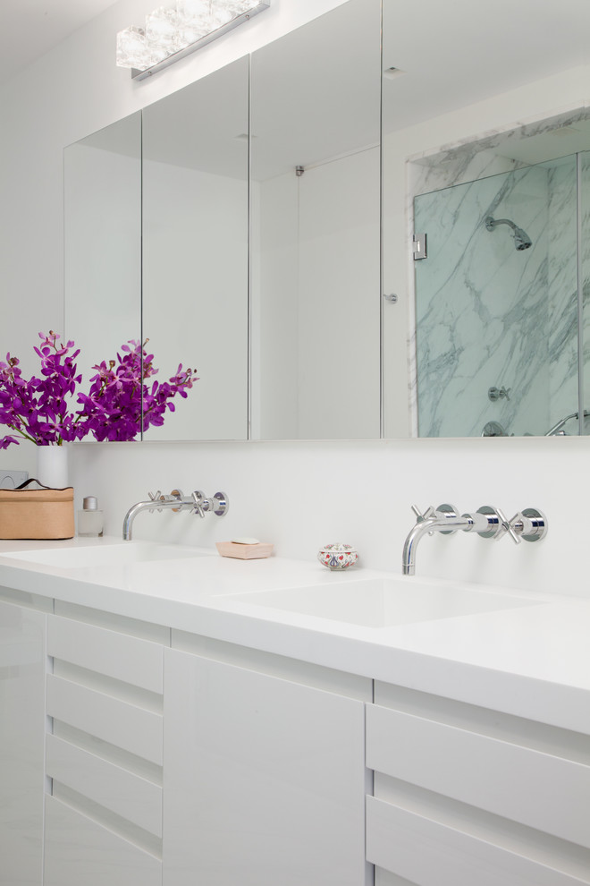 Bild på ett mellanstort funkis en-suite badrum, med ett integrerad handfat, släta luckor, vita skåp, bänkskiva i akrylsten, en dusch i en alkov, vit kakel, stenhäll och vita väggar