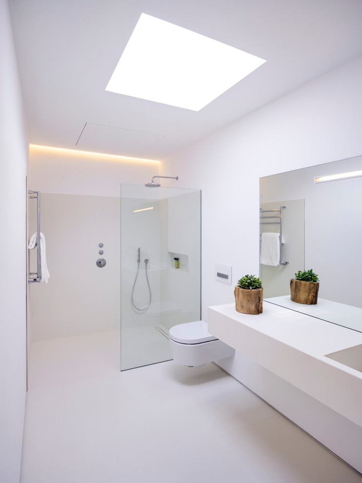 Modelo de cuarto de baño contemporáneo de tamaño medio con ducha a ras de suelo, sanitario de pared, paredes blancas, aseo y ducha y lavabo integrado