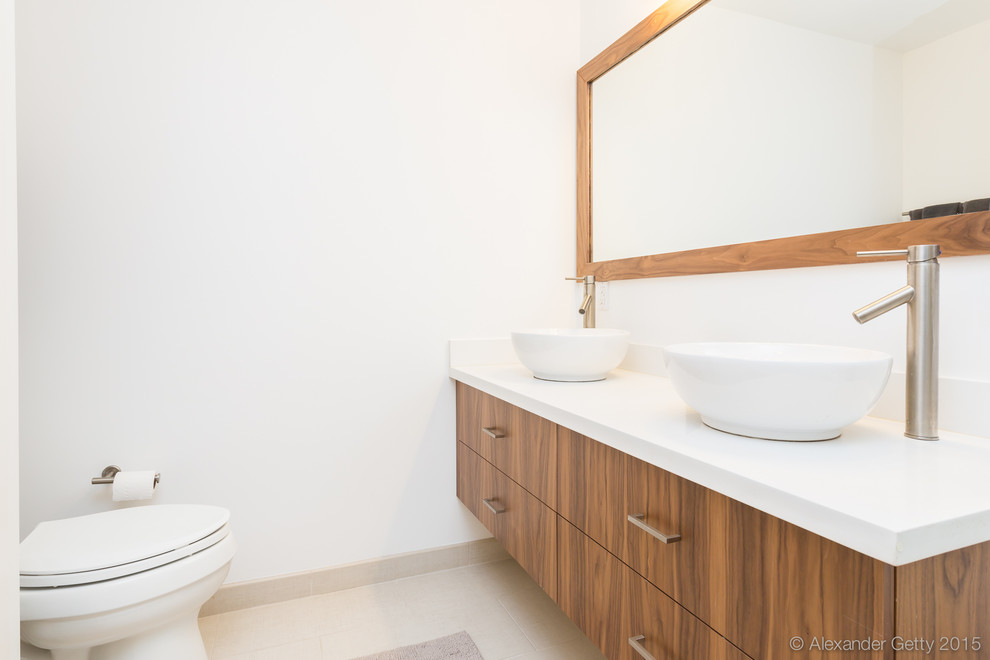 Modelo de cuarto de baño principal moderno pequeño con lavabo sobreencimera, armarios con paneles lisos, puertas de armario de madera oscura, sanitario de una pieza y paredes blancas
