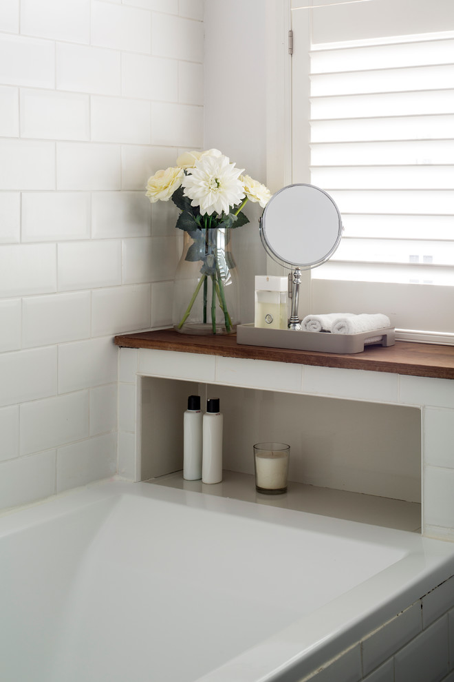 Réalisation d'une petite salle de bain design avec un placard à porte plane, une baignoire posée, un combiné douche/baignoire, un carrelage blanc, des carreaux de céramique, un mur blanc et un plan de toilette en bois.
