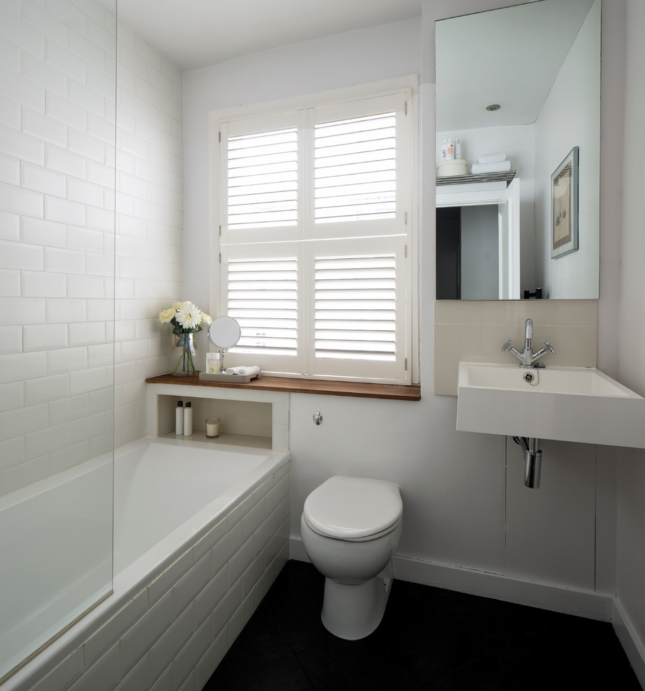 Kleines Modernes Badezimmer mit Einbaubadewanne, Duschbadewanne, Toilette mit Aufsatzspülkasten, weißen Fliesen, Keramikfliesen, weißer Wandfarbe, Keramikboden, Wandwaschbecken und Waschtisch aus Holz in Sussex