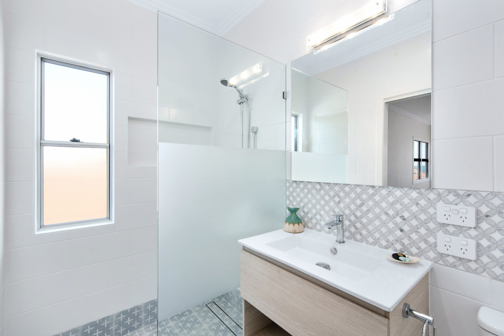 Стильный дизайн: маленькая ванная комната в стиле модернизм с светлыми деревянными фасадами, душевой комнатой, инсталляцией, разноцветной плиткой, керамической плиткой, белыми стенами, полом из керамической плитки, душевой кабиной, монолитной раковиной, разноцветным полом, открытым душем, белой столешницей, нишей, тумбой под одну раковину, подвесной тумбой и панелями на стенах для на участке и в саду - последний тренд