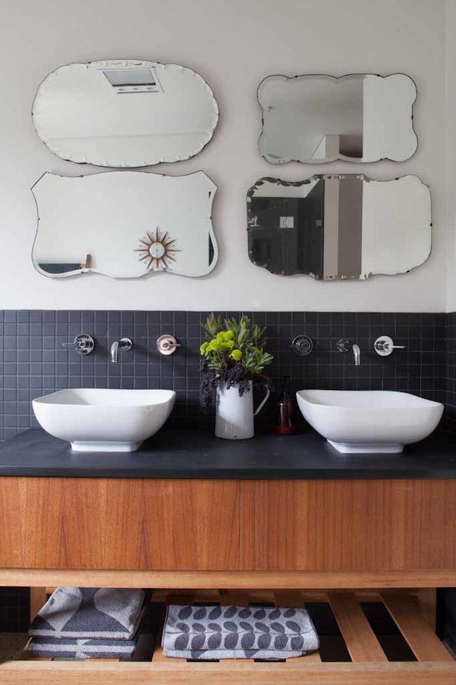 アデレードにあるコンテンポラリースタイルのおしゃれな浴室 (ベッセル式洗面器、オープンシェルフ、中間色木目調キャビネット、黒いタイル、黒い洗面カウンター) の写真