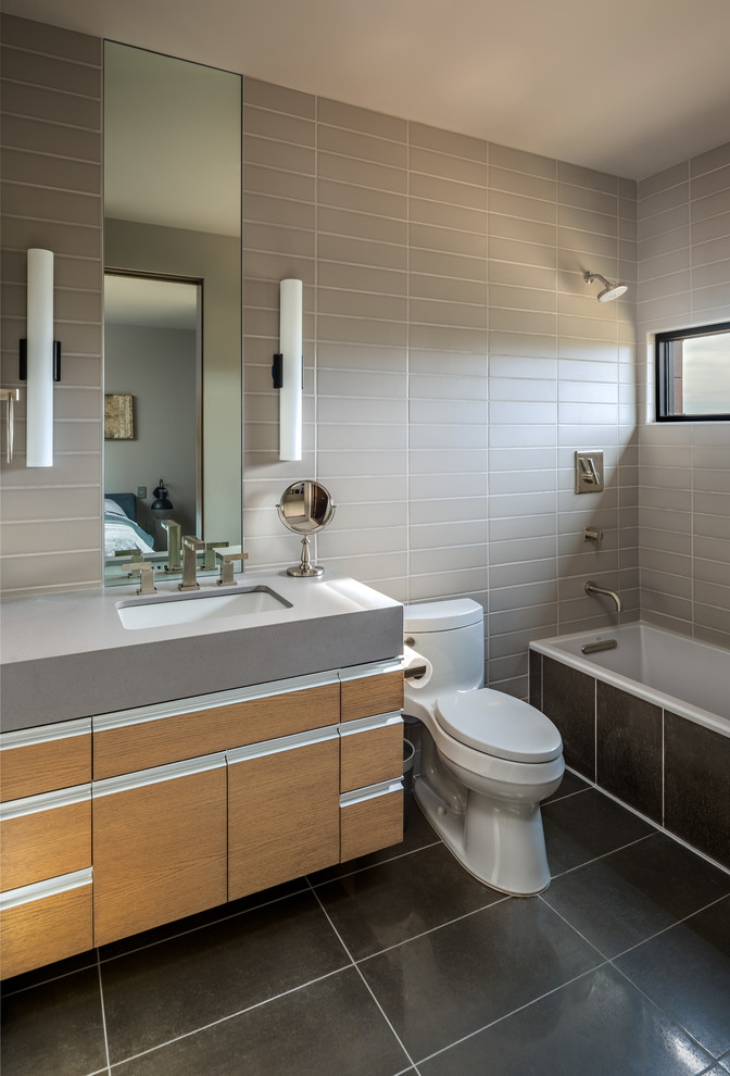 Idéer för ett modernt grå badrum med dusch, med släta luckor, skåp i mellenmörkt trä, ett badkar i en alkov, en dusch/badkar-kombination, en toalettstol med hel cisternkåpa, grå kakel, ett undermonterad handfat, grått golv, med dusch som är öppen, tunnelbanekakel och grå väggar