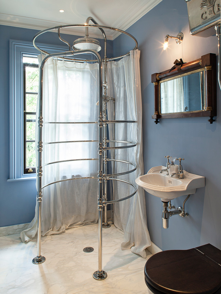 Klassisk inredning av ett badrum, med ett väggmonterat handfat, en öppen dusch, en toalettstol med hel cisternkåpa, blå väggar, marmorgolv och dusch med duschdraperi
