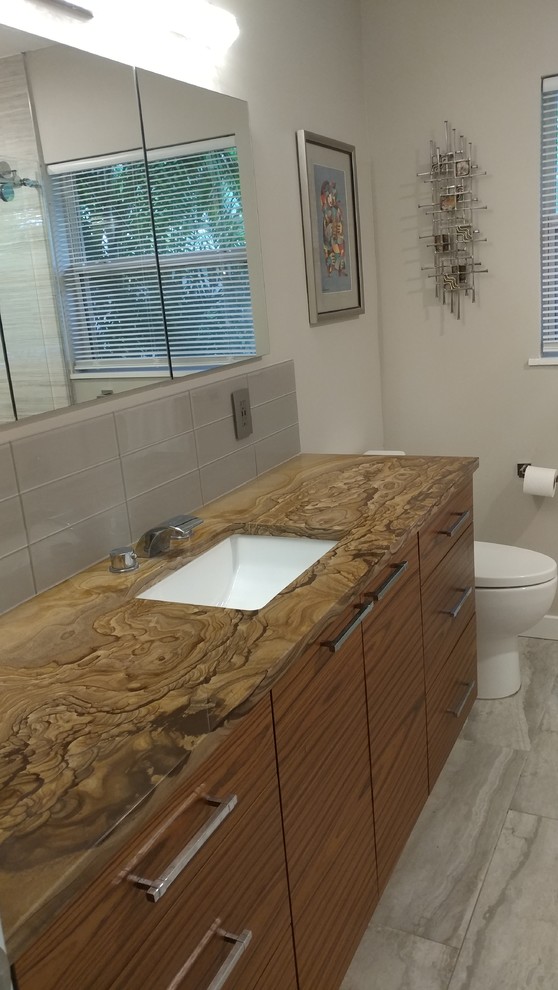 Medium sized contemporary bathroom in Tampa with flat-panel cabinets, medium wood cabinets, an alcove shower, a one-piece toilet, grey tiles, porcelain tiles, grey walls, porcelain flooring, a submerged sink, granite worktops, grey floors, a sliding door and brown worktops.