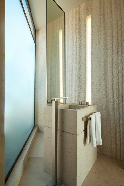 Inredning av ett modernt litet badrum, med en toalettstol med hel cisternkåpa, beige kakel, stenkakel, beige väggar, kalkstensgolv, ett piedestal handfat och bänkskiva i kalksten