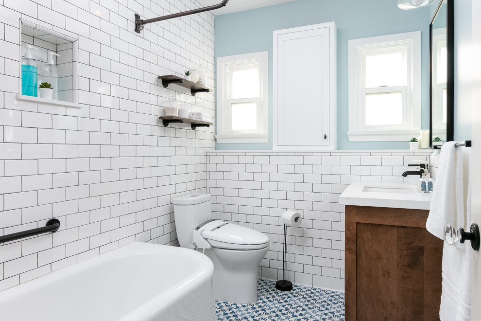 Cette photo montre une petite salle de bain éclectique en bois brun avec un placard à porte shaker, une baignoire d'angle, un combiné douche/baignoire, un carrelage blanc, un carrelage métro, un mur bleu, un sol en carrelage de porcelaine, un lavabo encastré, un plan de toilette en quartz modifié, un sol bleu, une cabine de douche avec un rideau, un plan de toilette blanc, une niche, meuble simple vasque, meuble-lavabo encastré et boiseries.