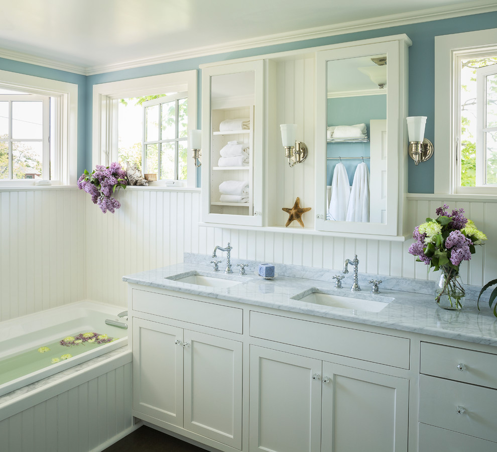 Example of a beach style master drop-in bathtub design in Portland Maine with shaker cabinets, white cabinets, an undermount sink, marble countertops and blue walls