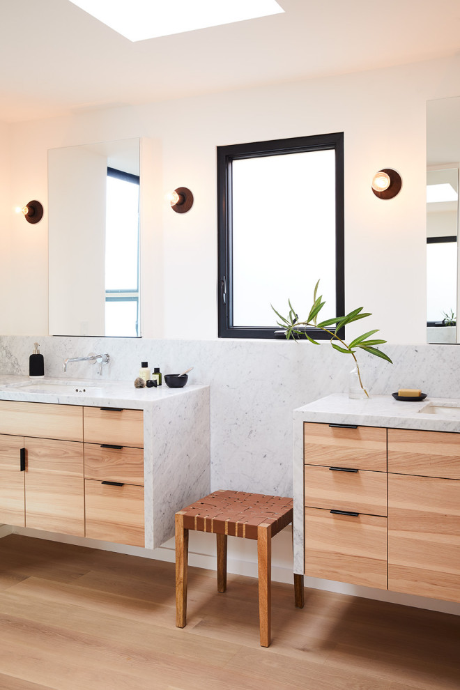 Imagen de cuarto de baño principal actual con armarios con paneles lisos, paredes blancas, suelo de madera clara, lavabo bajoencimera y encimera de mármol