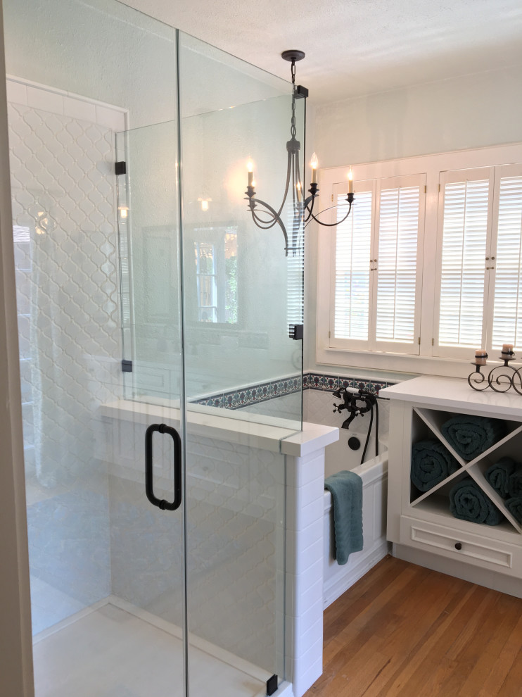 This is an example of a medium sized country ensuite bathroom in Sacramento with freestanding cabinets, white cabinets, a freestanding bath, a shower/bath combination, a two-piece toilet, white tiles, porcelain tiles, blue walls, light hardwood flooring, a submerged sink, quartz worktops, brown floors, a hinged door, white worktops, a single sink and a built in vanity unit.