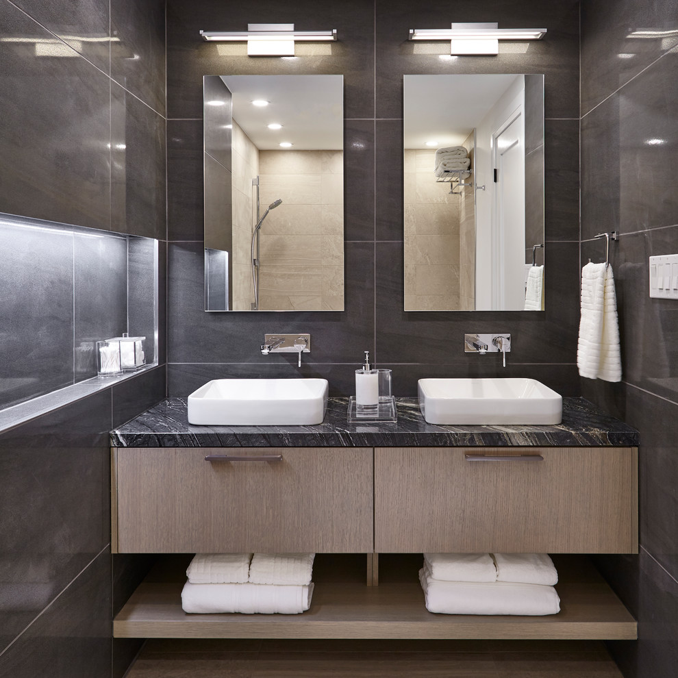 Пример оригинального дизайна: ванная комната среднего размера в стиле модернизм с плоскими фасадами, светлыми деревянными фасадами, накладной ванной, двойным душем, унитазом-моноблоком, серой плиткой, керамогранитной плиткой, серыми стенами, полом из керамогранита, душевой кабиной, настольной раковиной, столешницей из кварцита, душем с распашными дверями, серой столешницей и бежевым полом