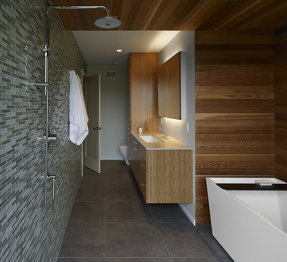 This is an example of a medium sized modern ensuite bathroom in San Francisco with a freestanding bath, mosaic tiles, a walk-in shower, an open shower, a one-piece toilet, grey walls, a submerged sink, grey floors, flat-panel cabinets, light wood cabinets, engineered stone worktops and white worktops.