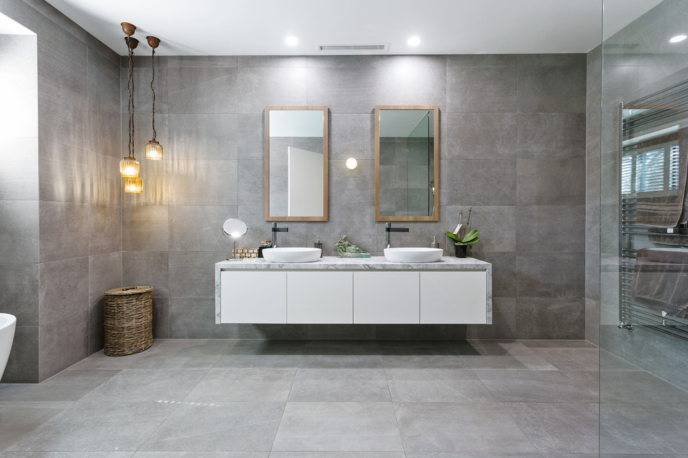 Exempel på ett mellanstort modernt vit vitt badrum med dusch, med släta luckor, skåp i mellenmörkt trä, en kantlös dusch, en toalettstol med separat cisternkåpa, vit kakel, vita väggar, betonggolv, ett väggmonterat handfat, granitbänkskiva, grått golv och dusch med gångjärnsdörr