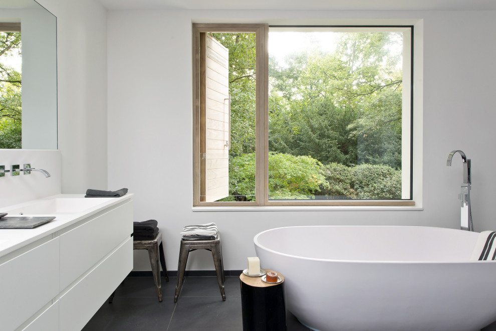 Inspiration for a medium sized contemporary ensuite bathroom in London with flat-panel cabinets, white cabinets, a freestanding bath, white walls, porcelain flooring, quartz worktops, black floors, white worktops and an integrated sink.