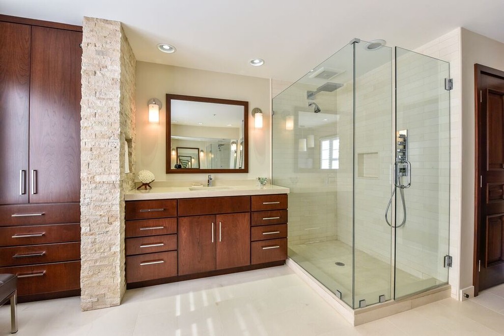 This is an example of a medium sized contemporary ensuite bathroom in DC Metro with flat-panel cabinets, medium wood cabinets, a two-piece toilet, beige tiles, stone tiles, beige walls, travertine flooring, a submerged sink, engineered stone worktops, an alcove shower, beige floors and a hinged door.